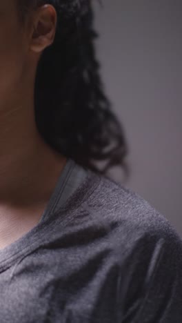 Vertical-Video-Close-Up-Studio-Shot-Of-Woman-Wearing-Sports-Clothing-Against-Dark-Background-Warming-Up